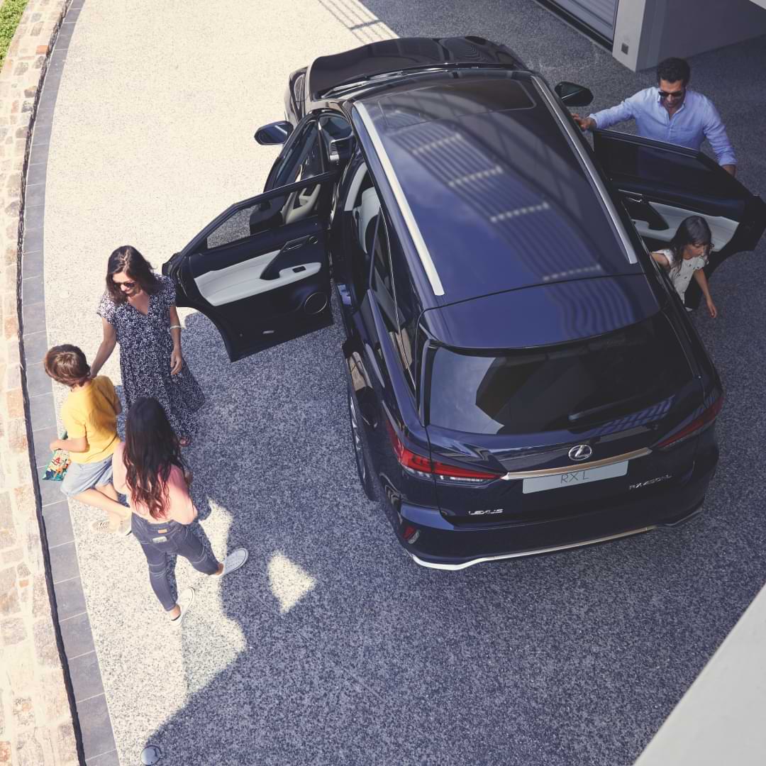 A family pile out of a Lexus RX L - father, mother and three children. The sun is shining.