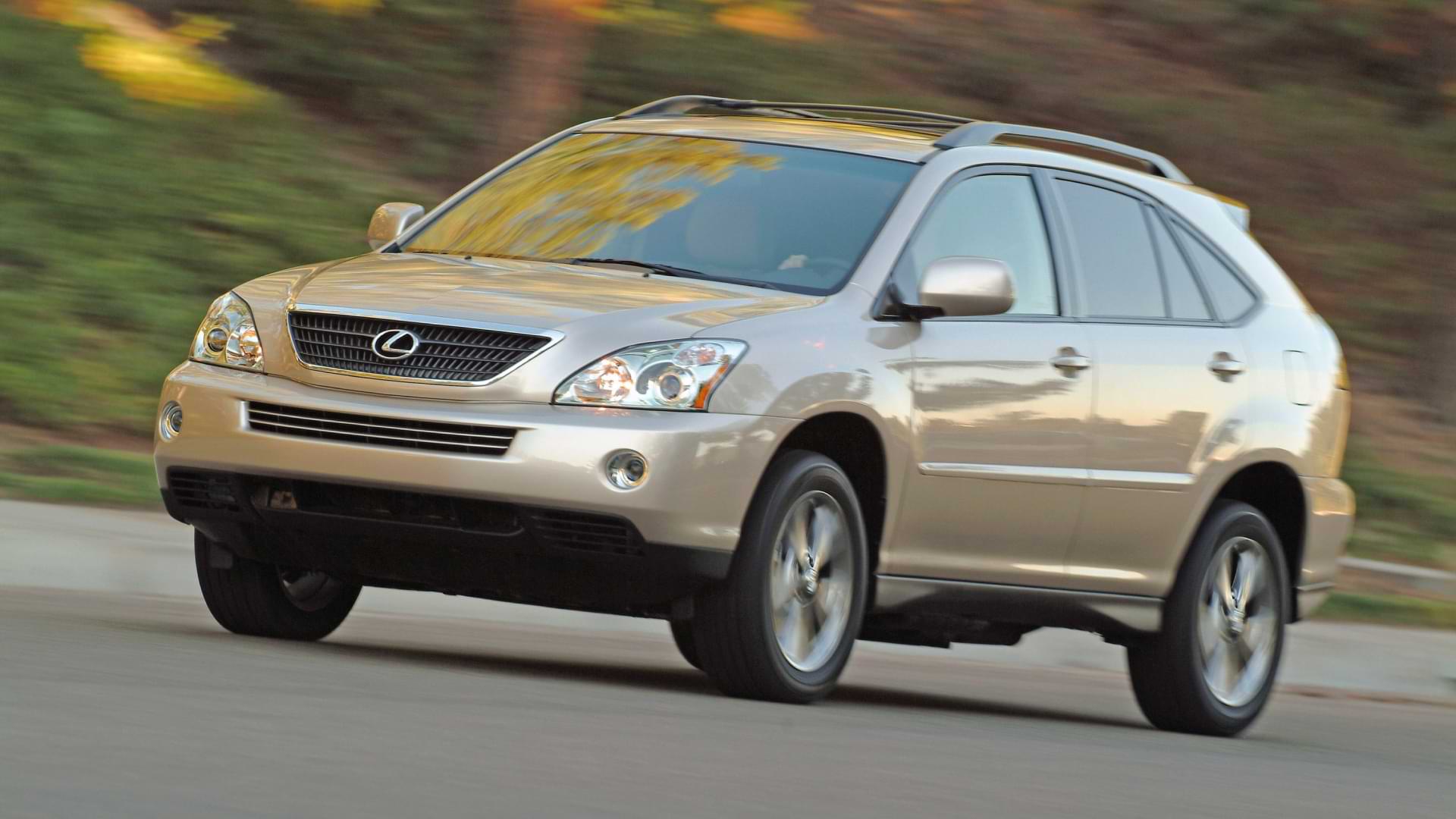 The world's first electrified luxury crossover, the Lexus RX hybrid - a gold RX Hybrid drives at speed, trees in the background.
