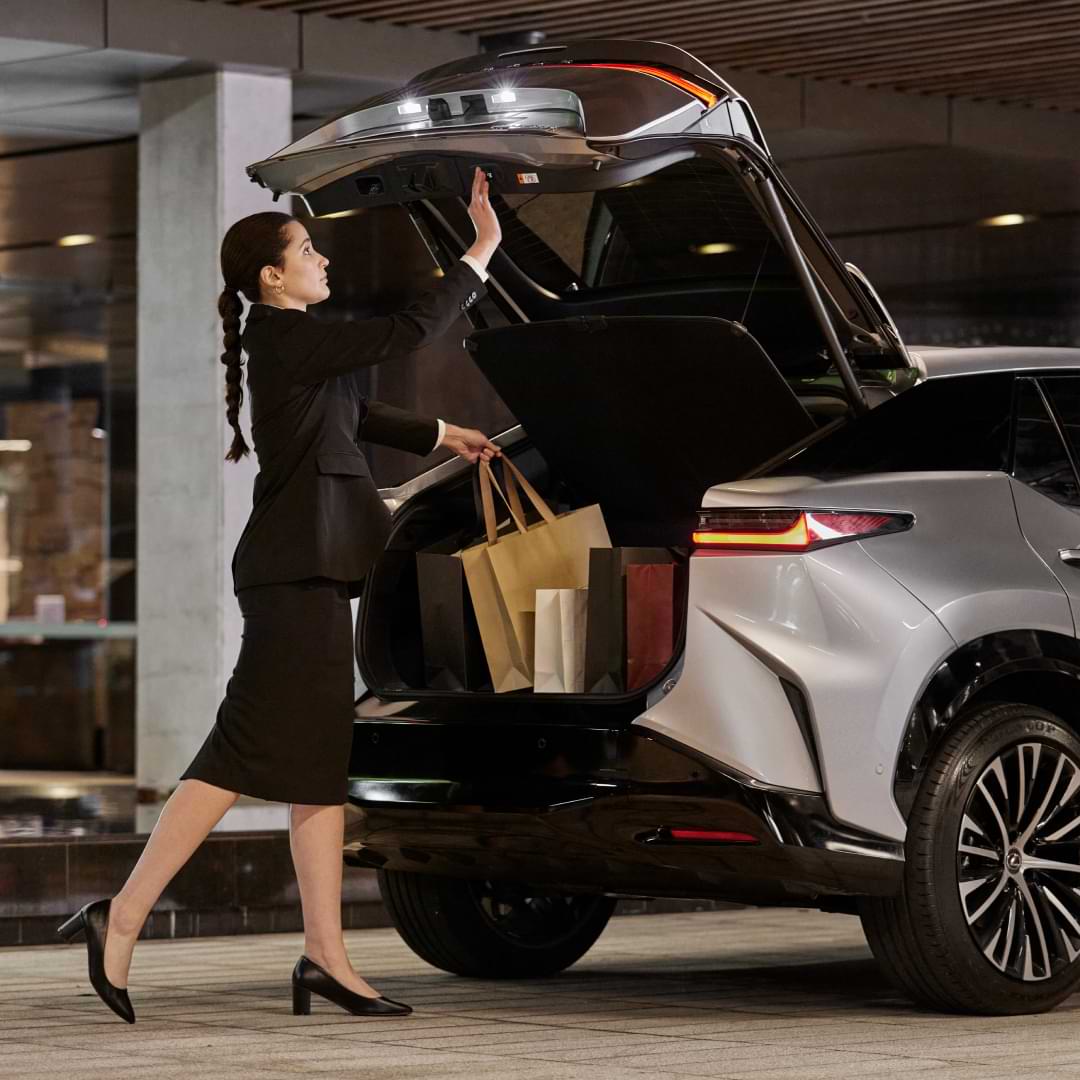 A valet places shopping bags into the open boot of a Lexus vehicle.