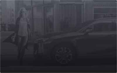 A woman stands next to a Lexus car on an urban street.