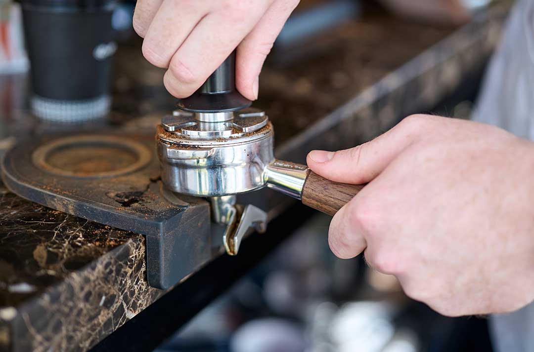 A barista presses ground coffee into a portafilter on a café counter.