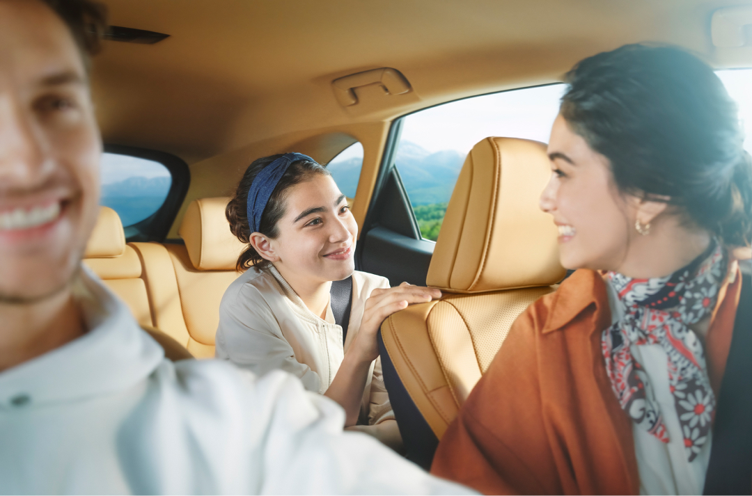 A family in a Lexus NX smiling, man drives, woman in the passenger seat, turns around to a young girl in the back