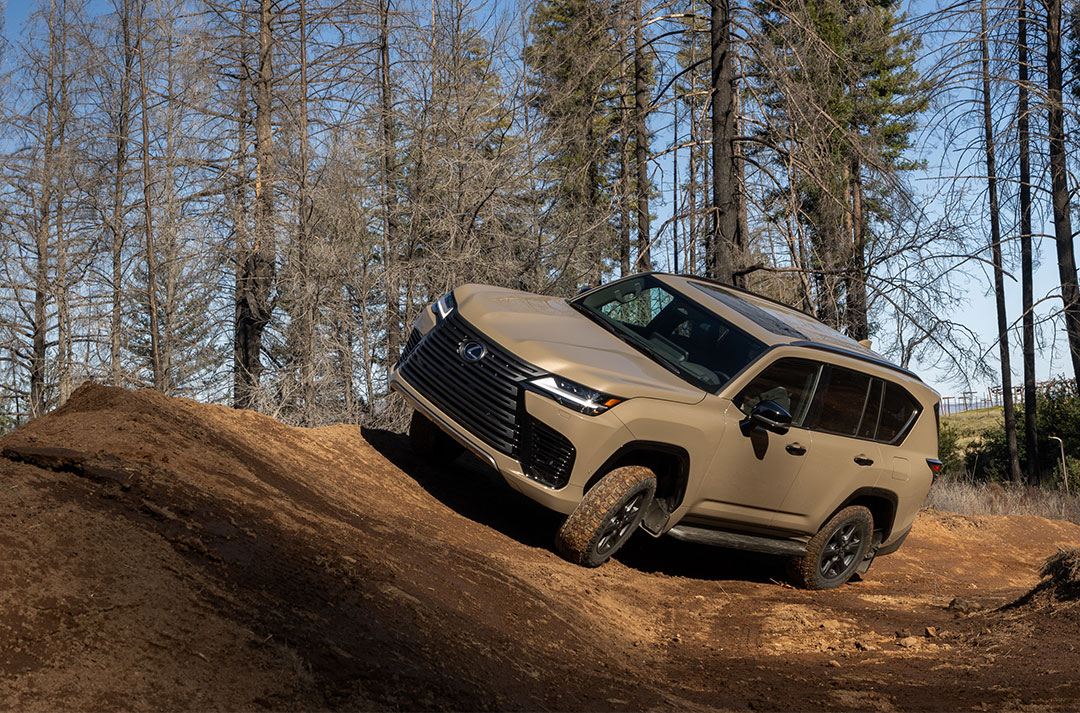 A tan Lexus LX SUV driving cross country with trees in the background