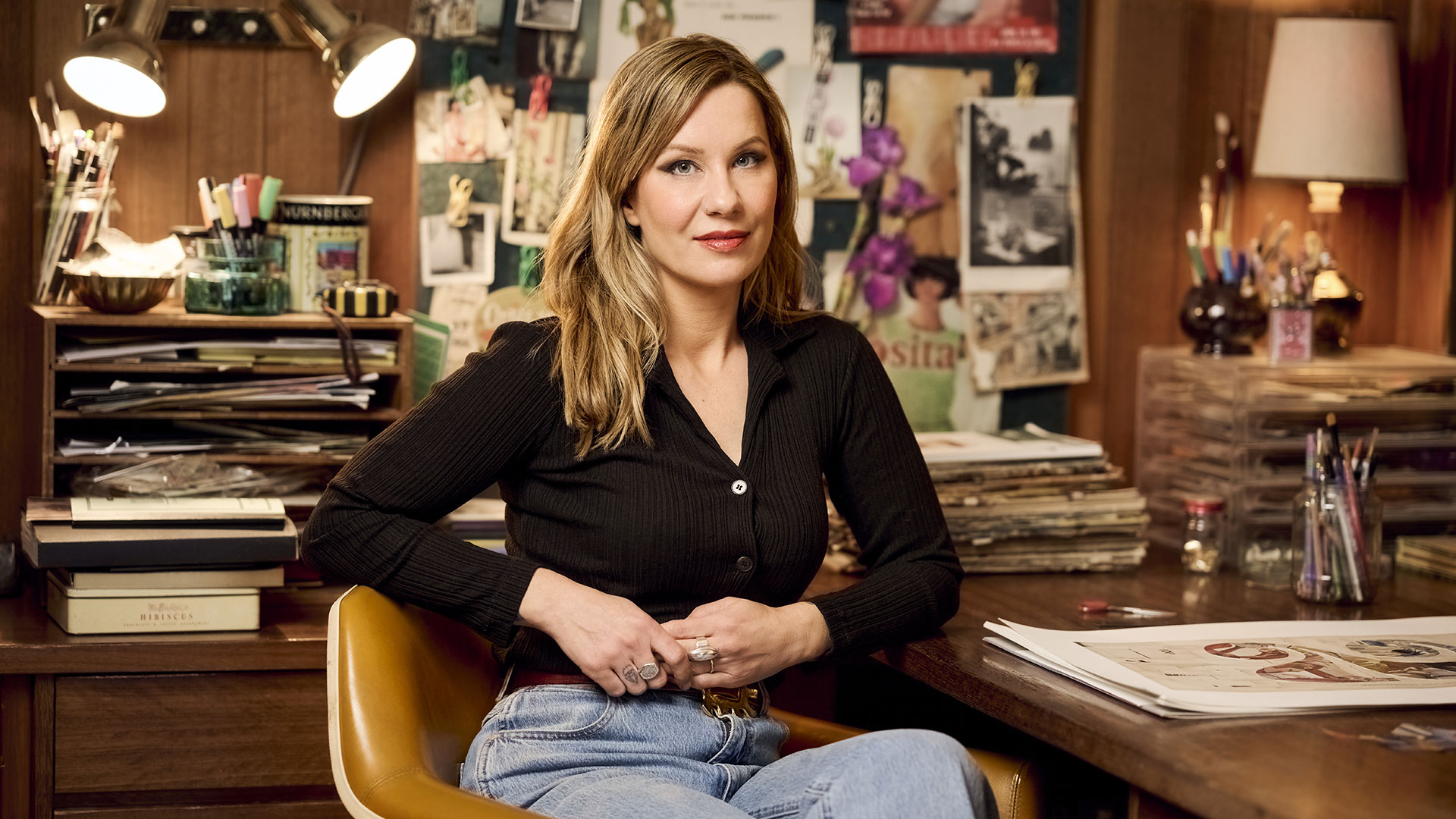Artist Simone Esterhuizen seated at a desk with artworks and creative materials behind her