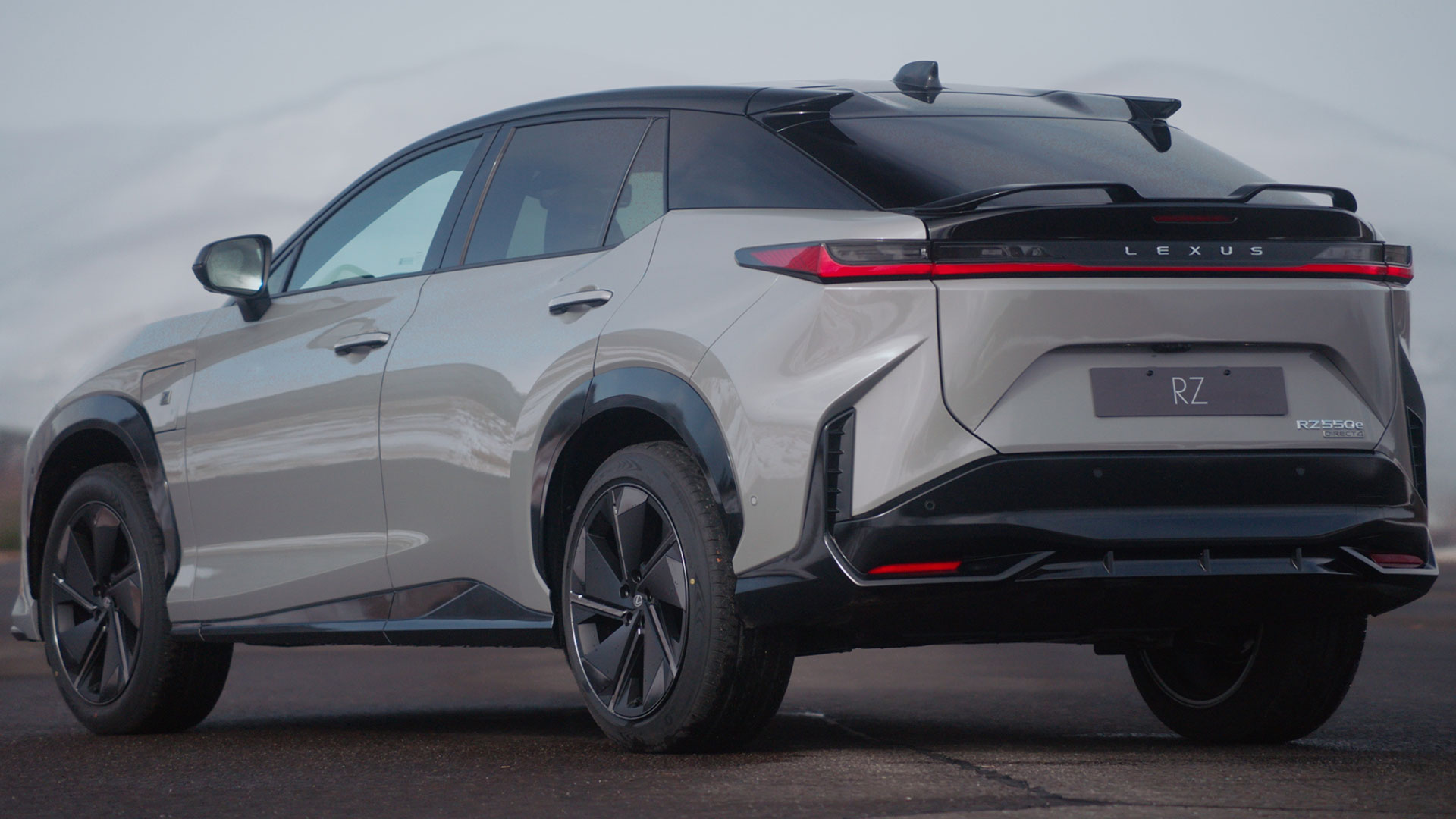 Rear three-quarter view of a silver Lexus RZ electric SUV with a black roof.