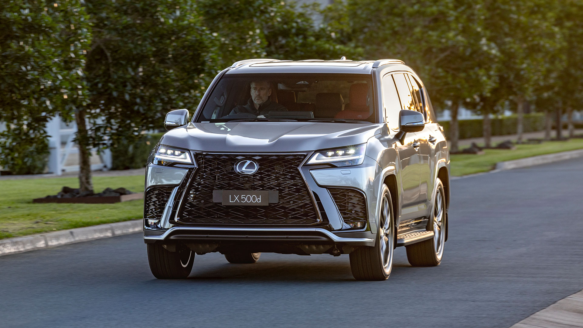 A 2025 Lexus LX 500d F Sport in grey, driving down a residential street 