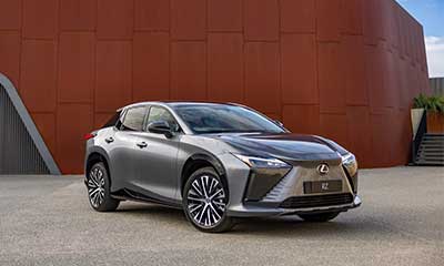 Silver Lexus RZ, battery electric vehicle in front of modern building.